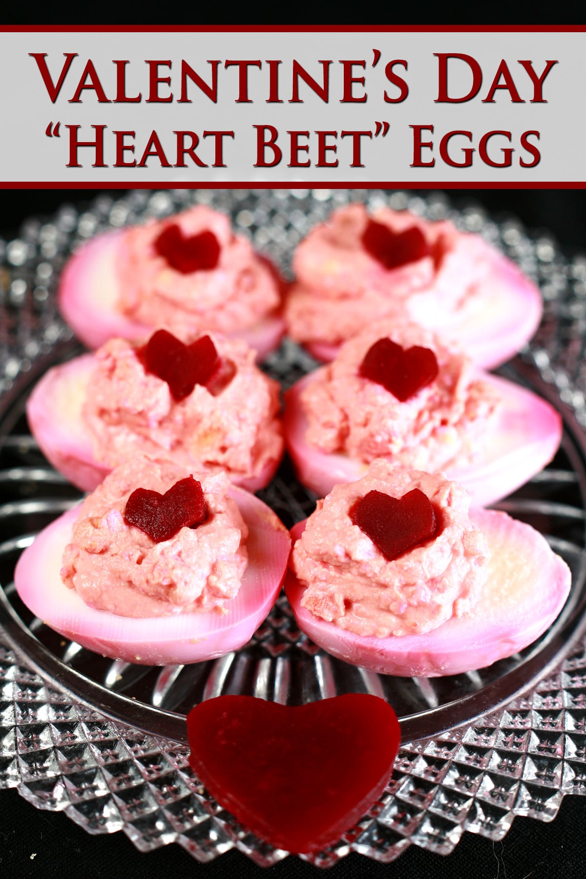 6 pink tie dyed deviled eggs on a glass plate.  Each is topped with a heart shaped piece of pickled beet.