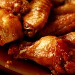 A close up view of a pile of honey garlic glazed wings on a small brown plate.