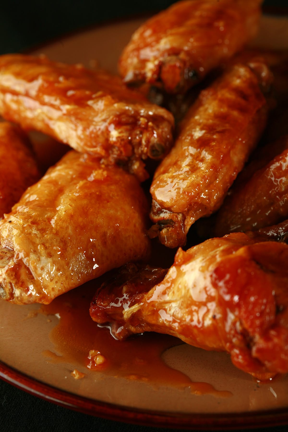 A close up view of a pile of honey garlic wings on a small brown plate.