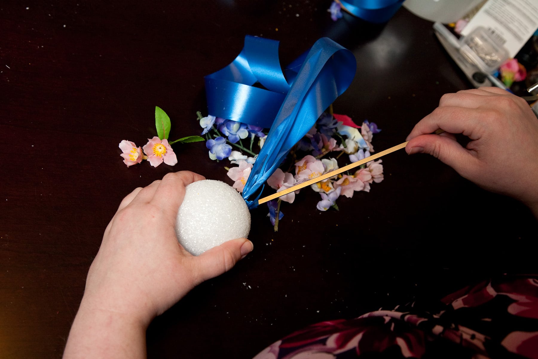 A chopstick is being used to poke a ribbon through a styrofoam ball.