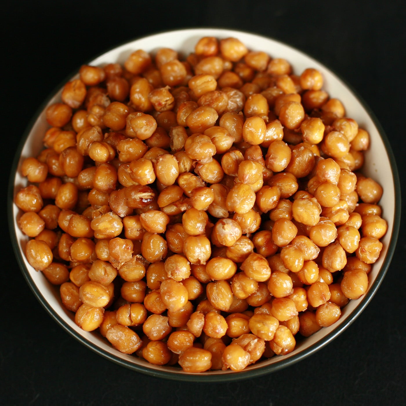 A shallow white and black bowl, piled high with roasted garbanzo beans.