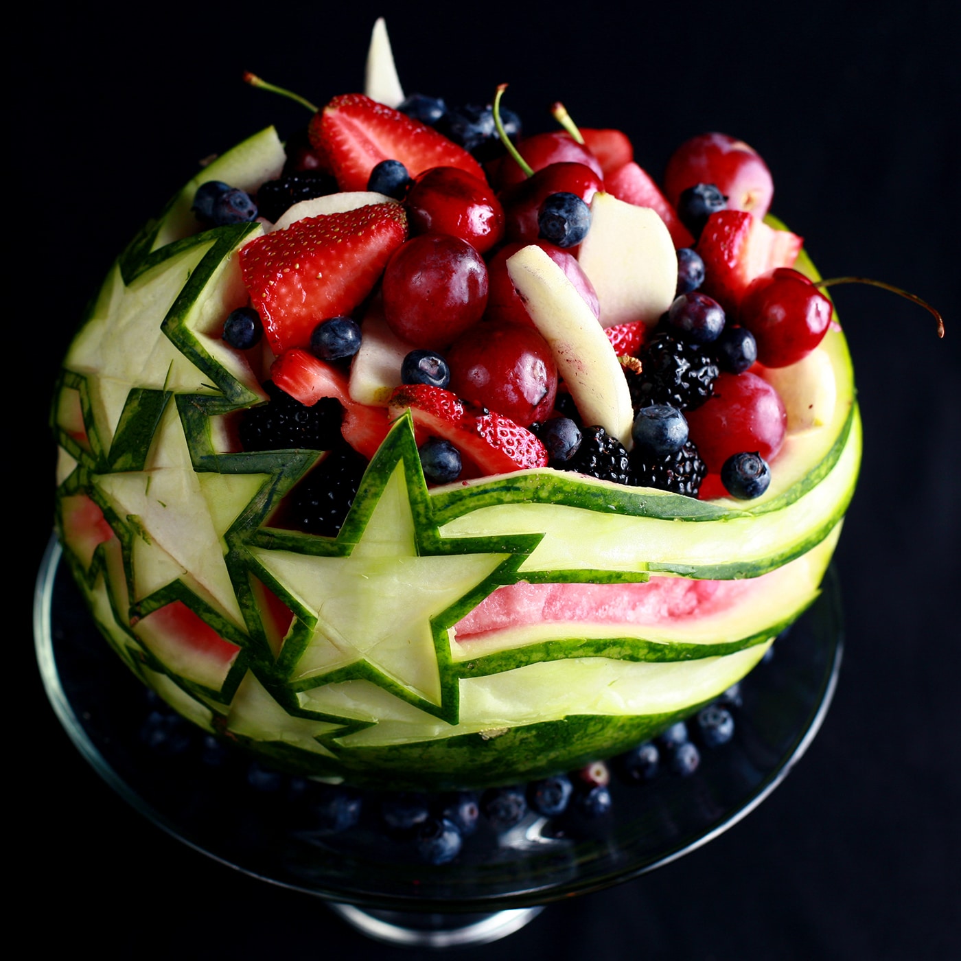 An Independence Day Watermelon Bowl. It is carved with a stars and stripes design, and filled with red, white, and blue fruit.