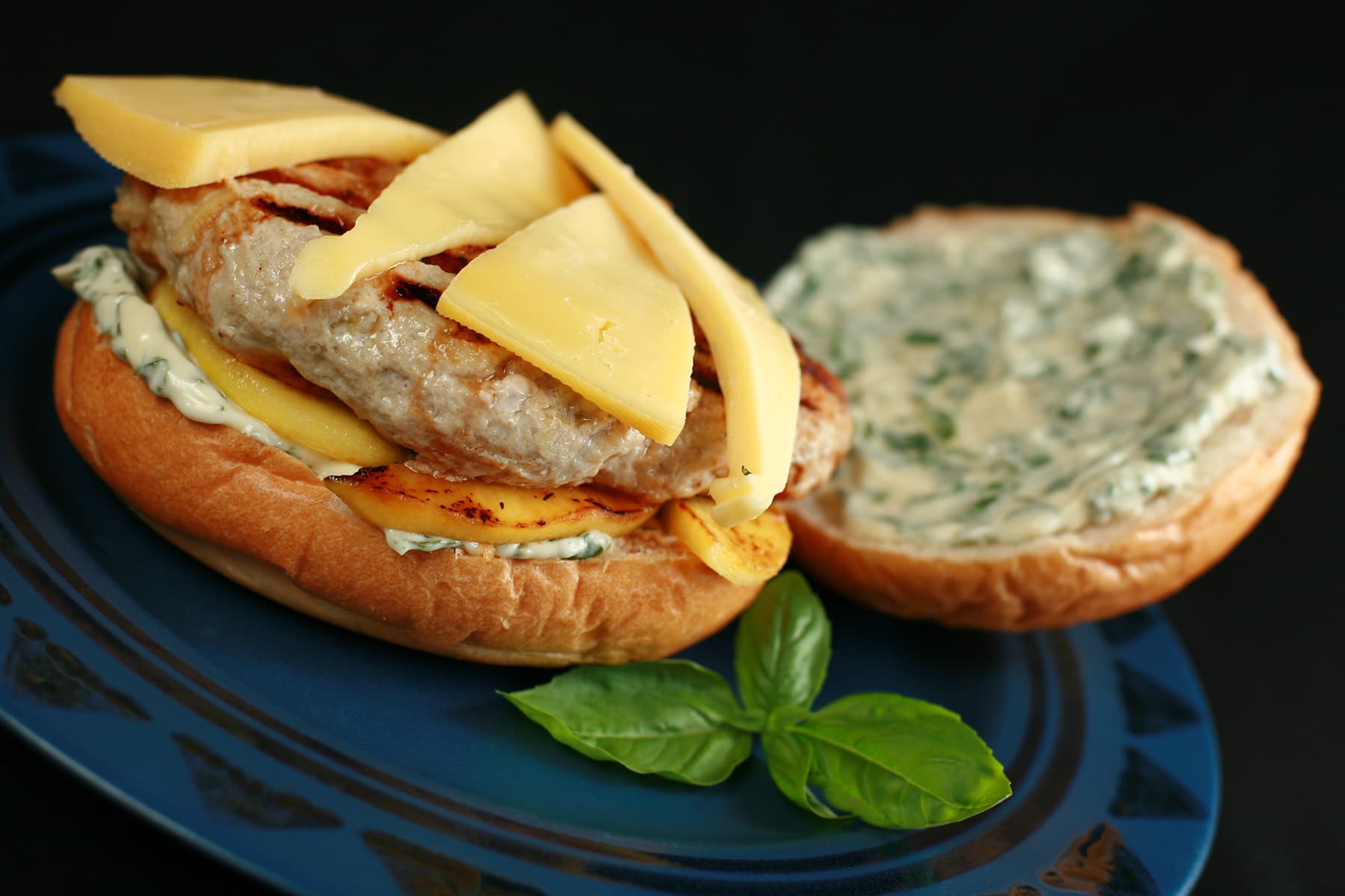 An apple chicken burger with slices of gouda cheese and spread with basil mayonnaise, on a blue plate.