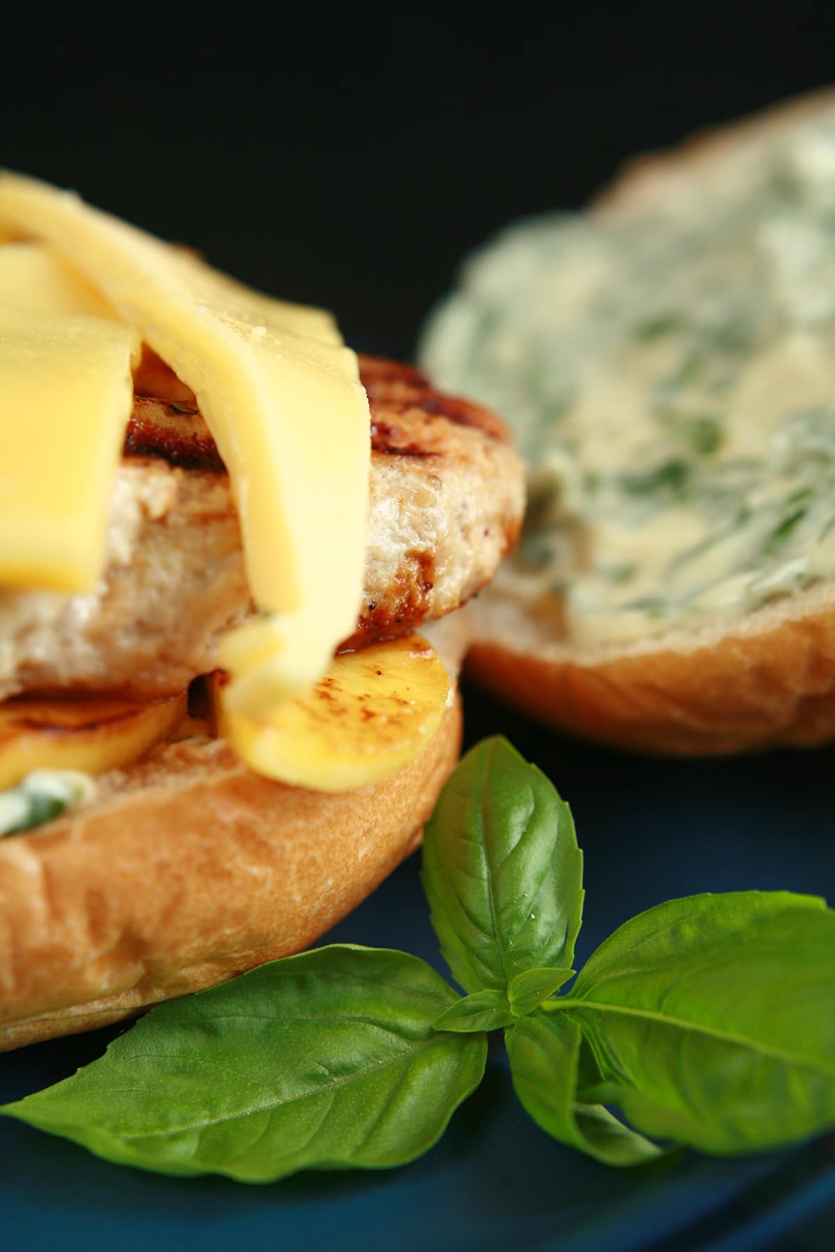 An apple chicken burger with slices of gouda cheese and spread with basil mayonnaise, on a blue plate.