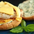 An apple chicken burger with slices of gouda cheese and spread with basil mayonnaise, on a blue plate.