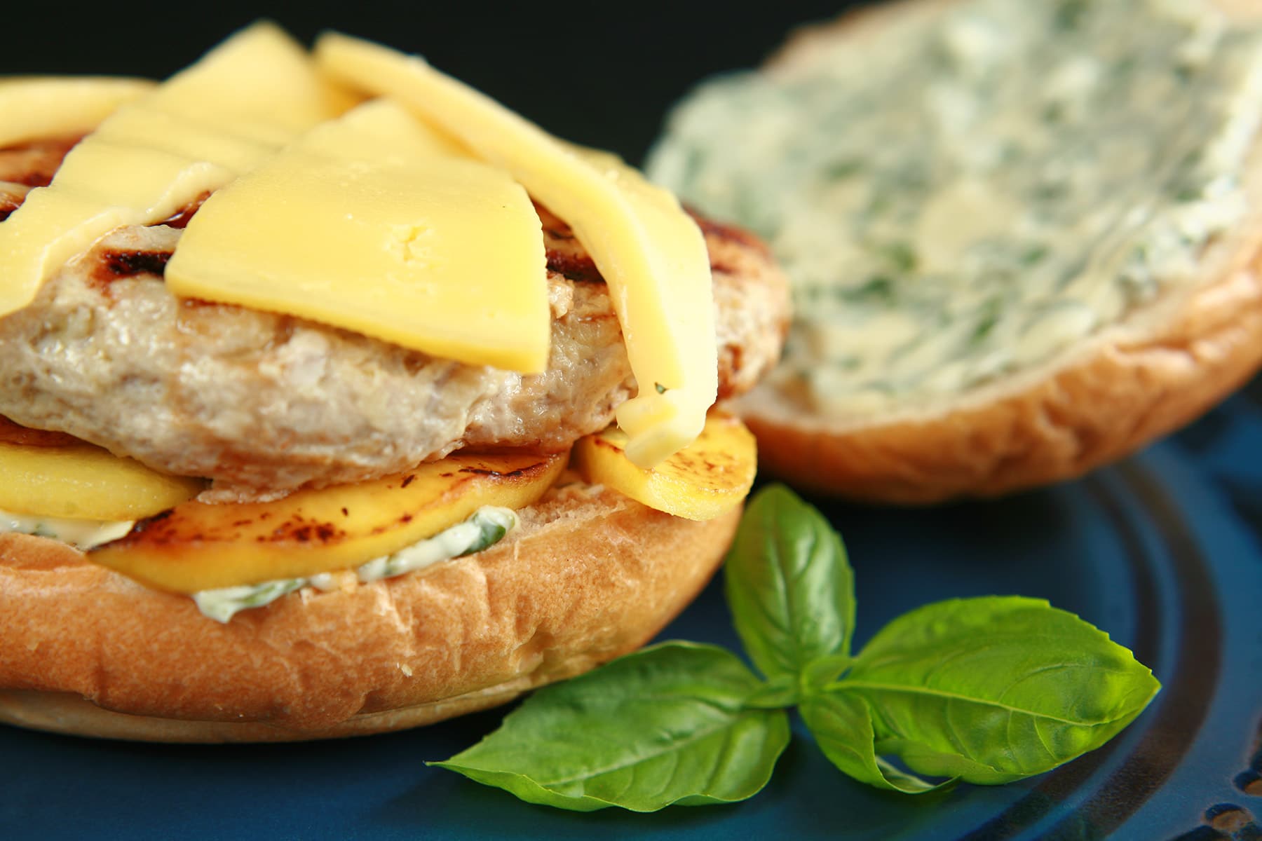 An apple chicken burger with slices of gouda cheese and spread with basil mayonnaise, on a blue plate.