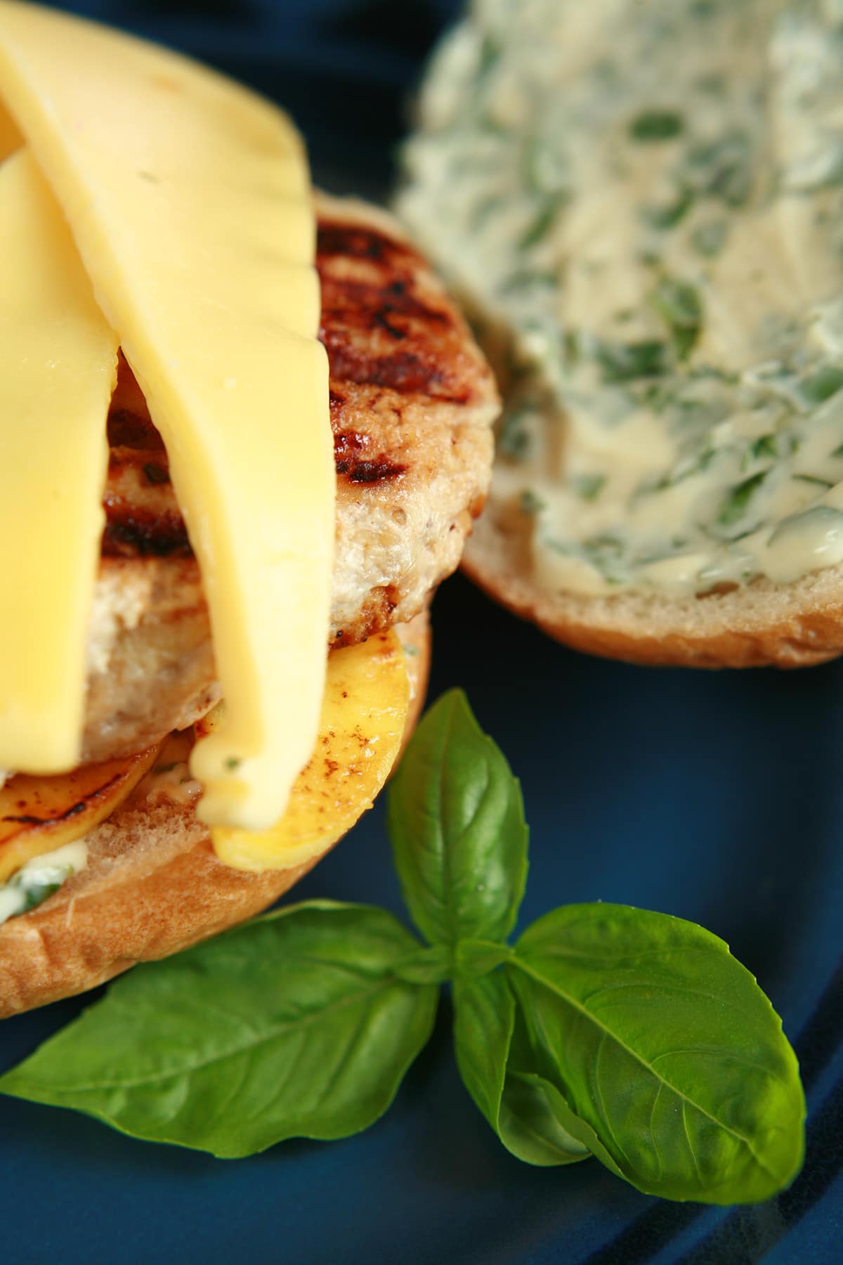 An apple chicken burger with slices of gouda cheese and spread with basil mayonnaise, on a blue plate.