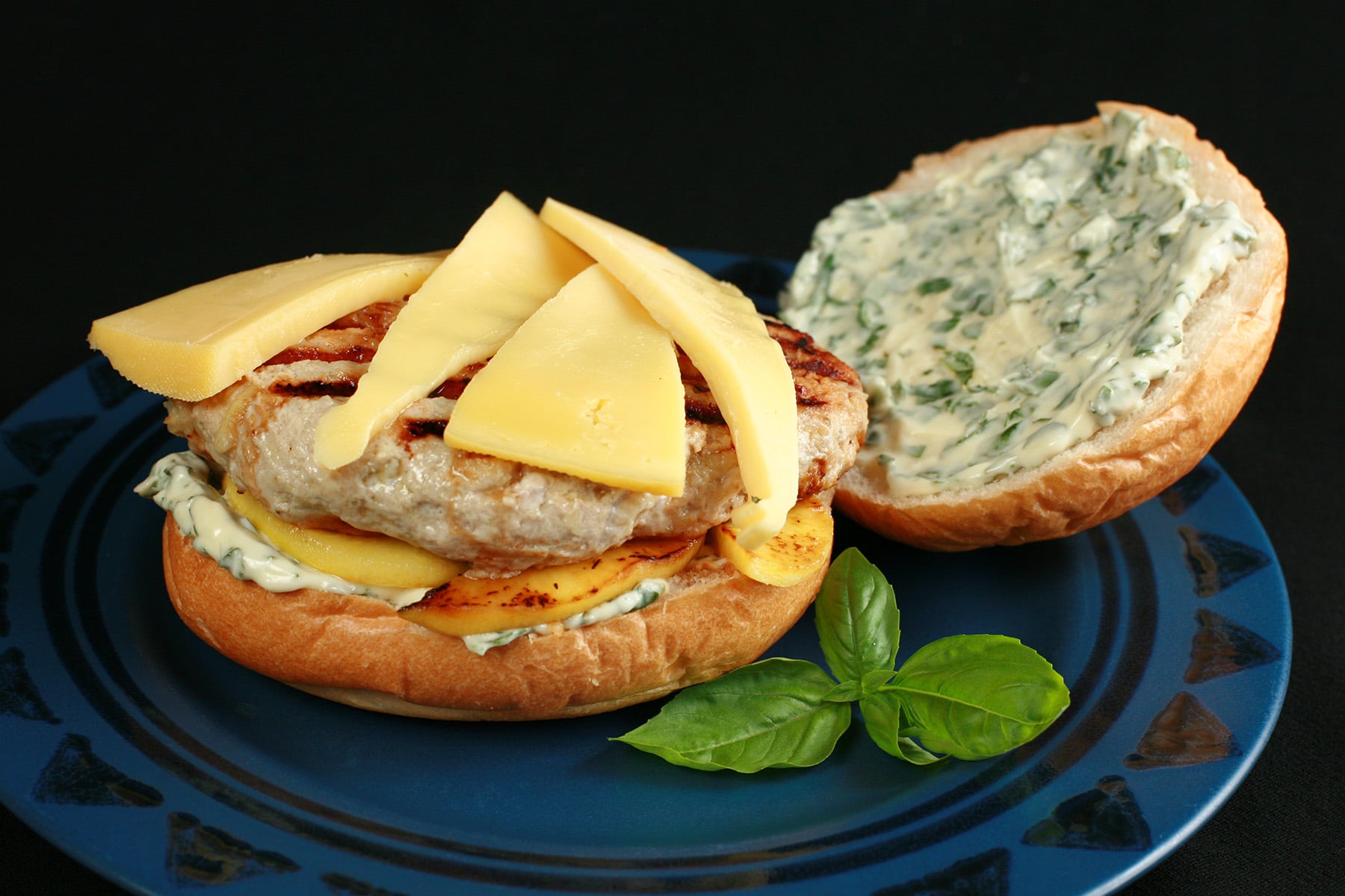 An apple chicken burger with slices of gouda cheese and spread with basil mayonnaise, on a blue plate.