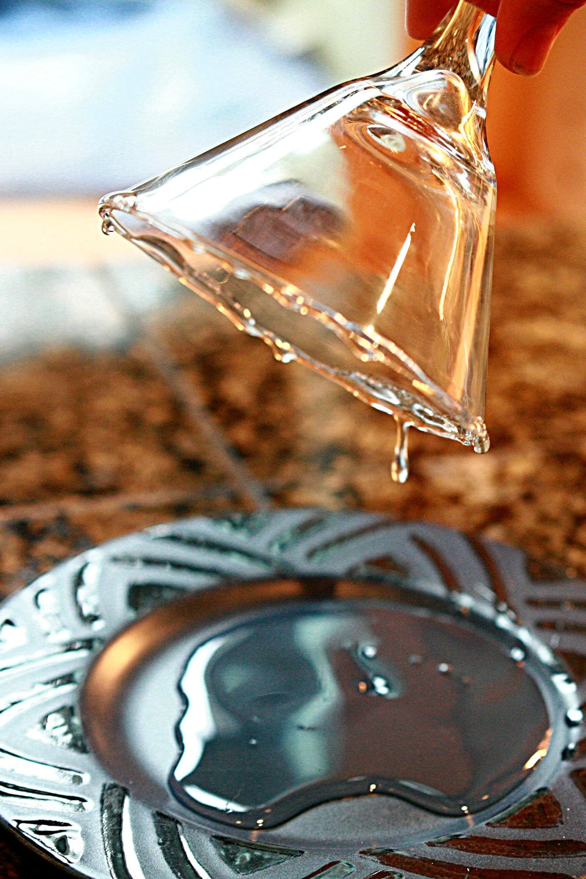 A hand holds a martini glass upside down over a blue plate, allowing excess corn syrup to drip off.