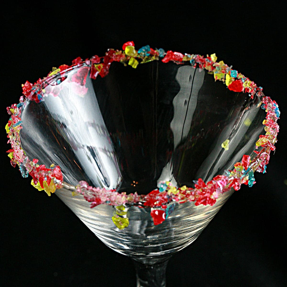 A martini glass with a candied cocktail rim, against a black background.