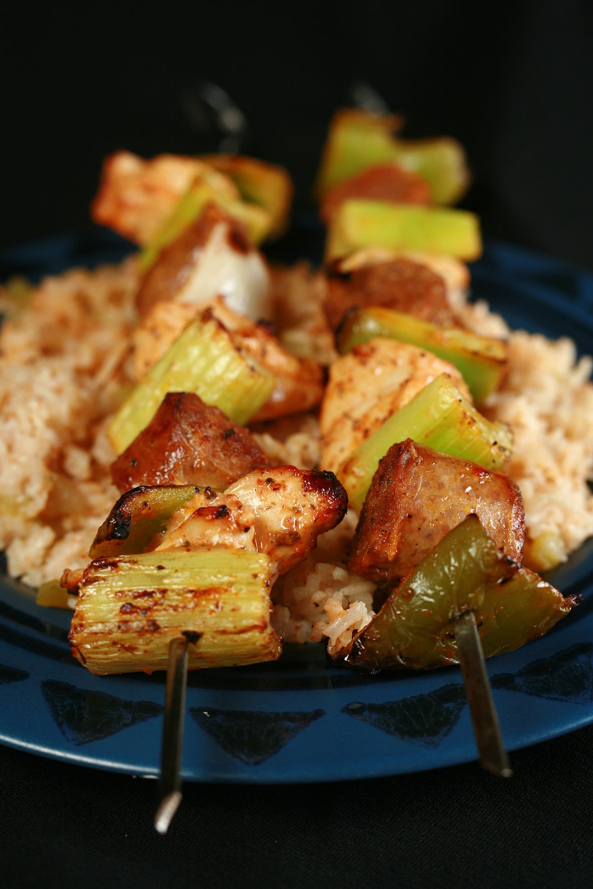 Two grilled jambayala skewers of chicken, sausage, green onions, onion, and celery on a bed of intensely seasoned "dirty" rice.