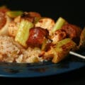 Two grilled skewers of chicken, sausage, green onions, onion, and celery on a bed of intensely seasoned "dirty" rice.