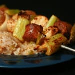 Two grilled skewers of chicken, sausage, green onions, onion, and celery on a bed of intensely seasoned "dirty" rice.