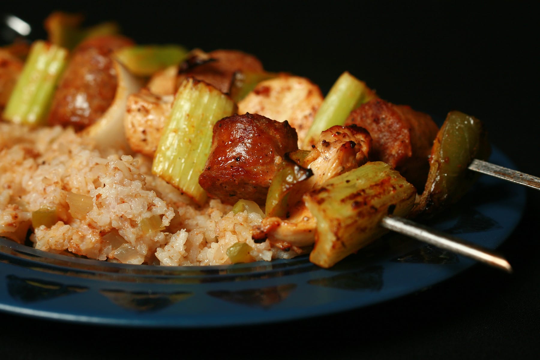 Two grilled skewers of chicken, sausage, green onions, onion, and celery on a bed of intensely seasoned "dirty" rice.