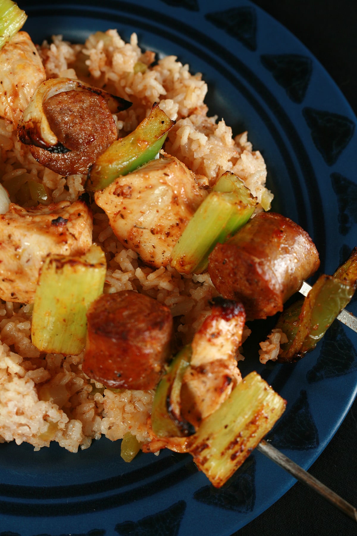 Two grilled jambayala skewers of chicken, sausage, green onions, onion, and celery on a bed of intensely seasoned "dirty" rice.