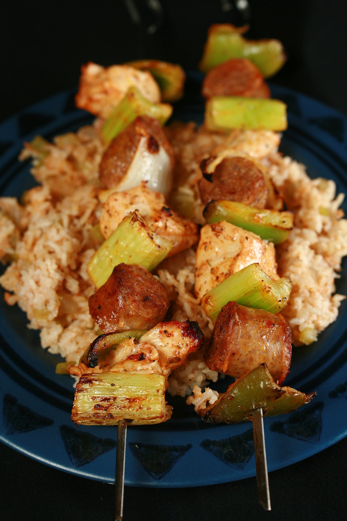 Two grilled jambayala skewers of chicken, sausage, green onions, onion, and celery on a bed of intensely seasoned "dirty" rice.