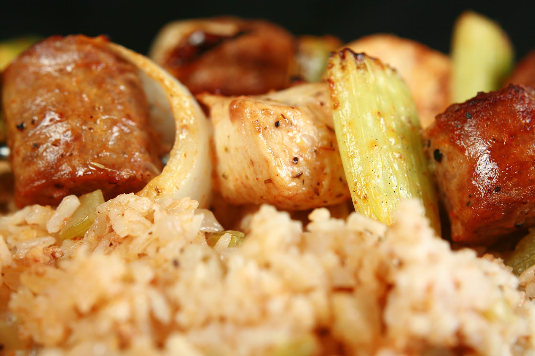 Two grilled skewers of chicken, sausage, green onions, onion, and celery on a bed of intensely seasoned "dirty" rice.