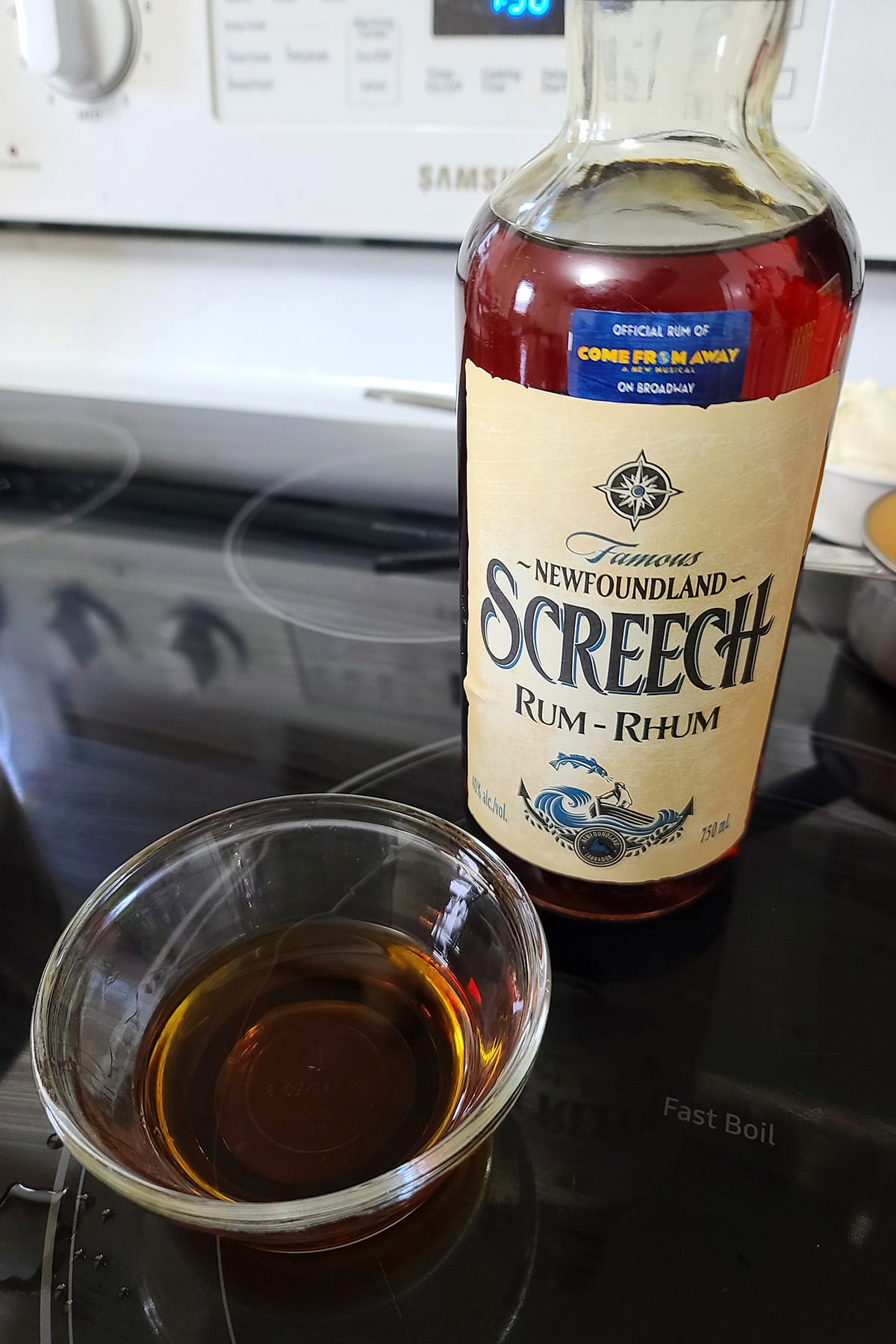 A bottle of Screech rum, behind a small glass bowl with rum in it.