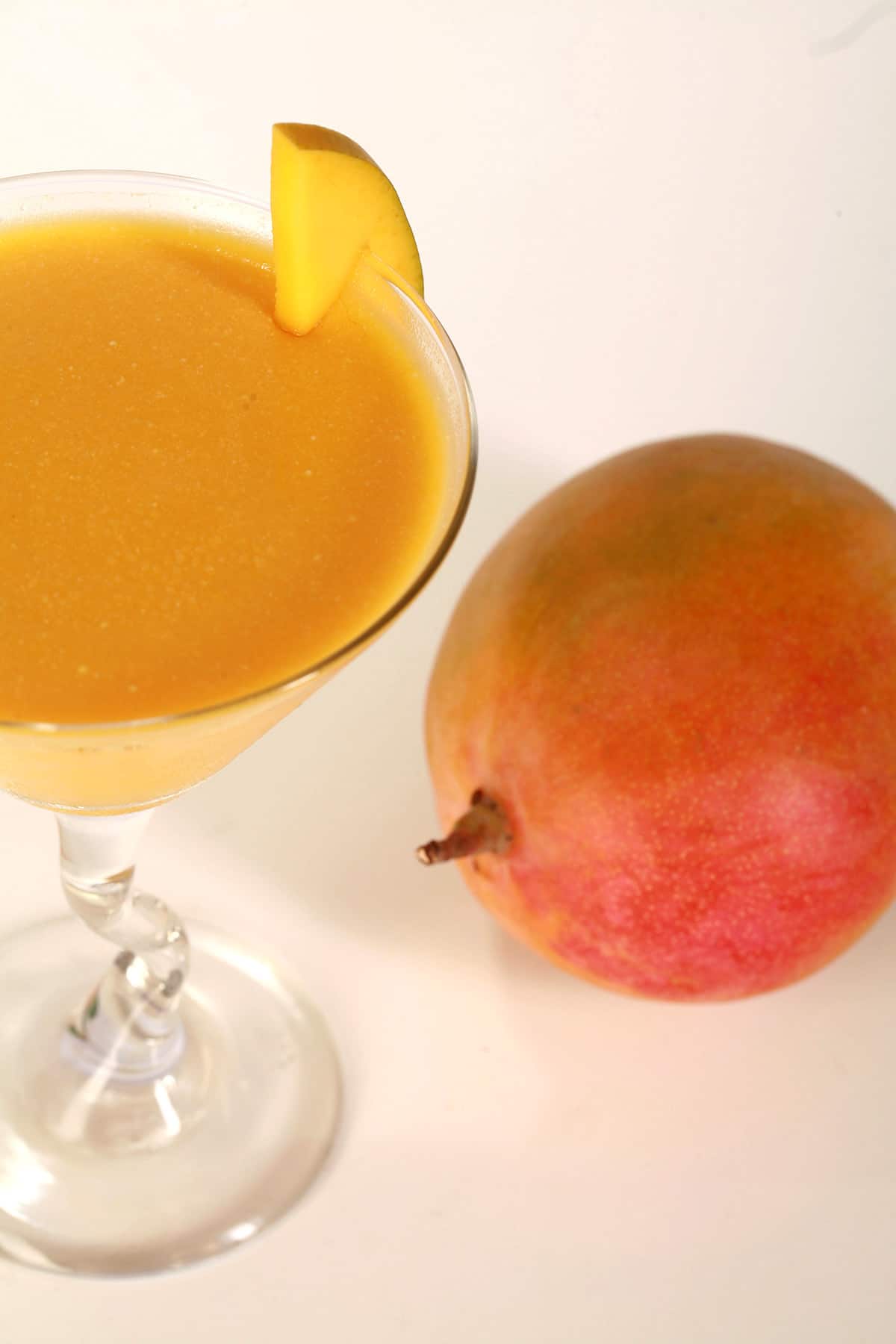 A martini glass of mango daiquiri panna cotta, with a whole mango next to it.