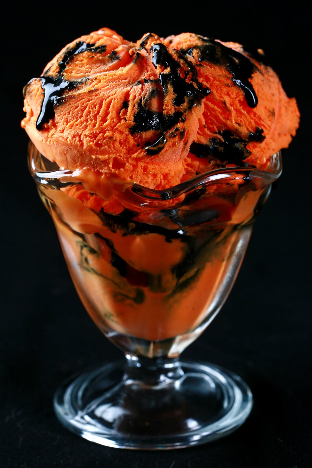 A fluted glass dessert bowl with 2 big scoops of Tiger Tail Ice Cream - Orange ice cream with a licorice ribbon throughout.