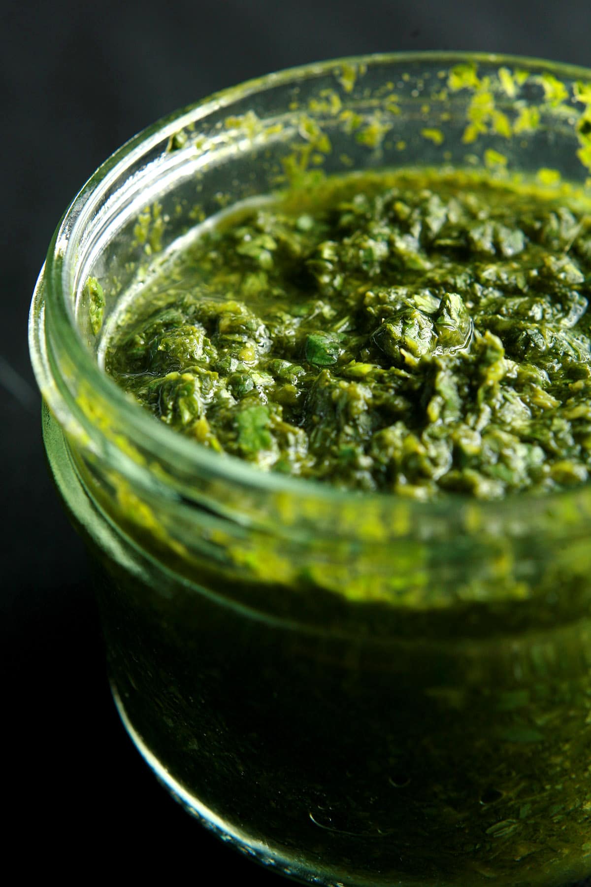 A close up view of a jar of cilantro mint chutney, a deep green dip that looks like pesto.