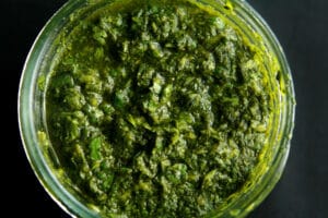 A close up view of a jar of cilantro mint chutney, a deep green dip that looks like pesto.