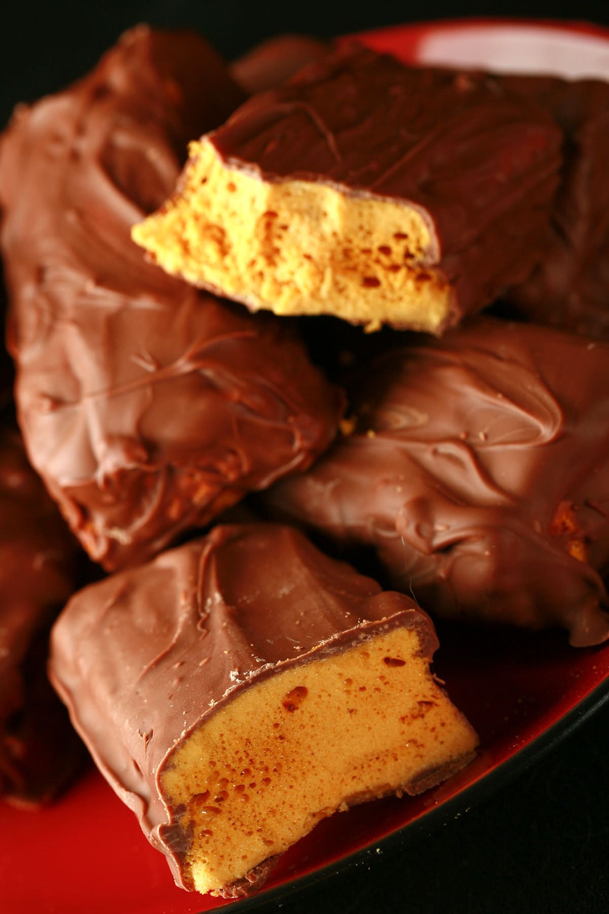 A small red plate is piled high with homemade crunchie bars. One is broken in half to reveal the sponge toffee inside.