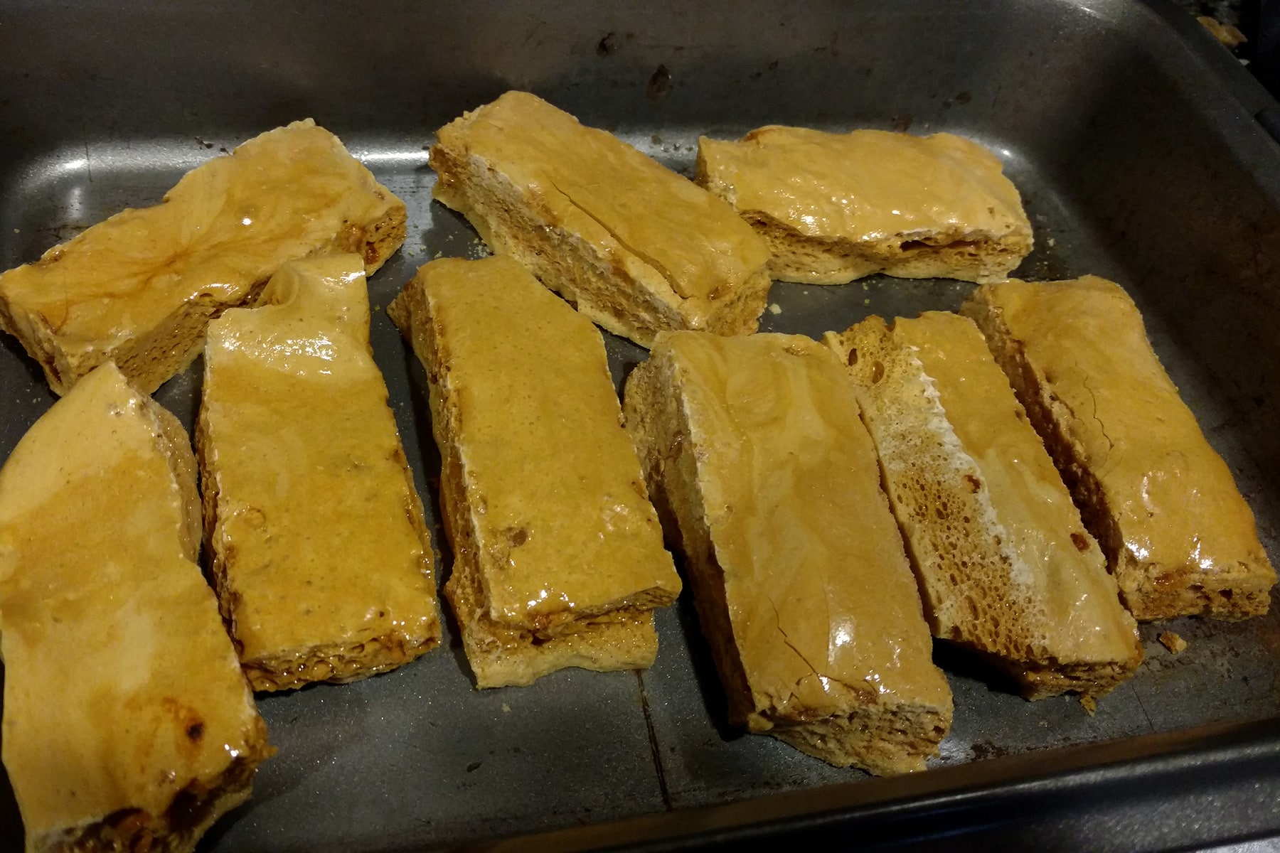 Several long, narrow bars of sponge toffee, arranged in a pan.