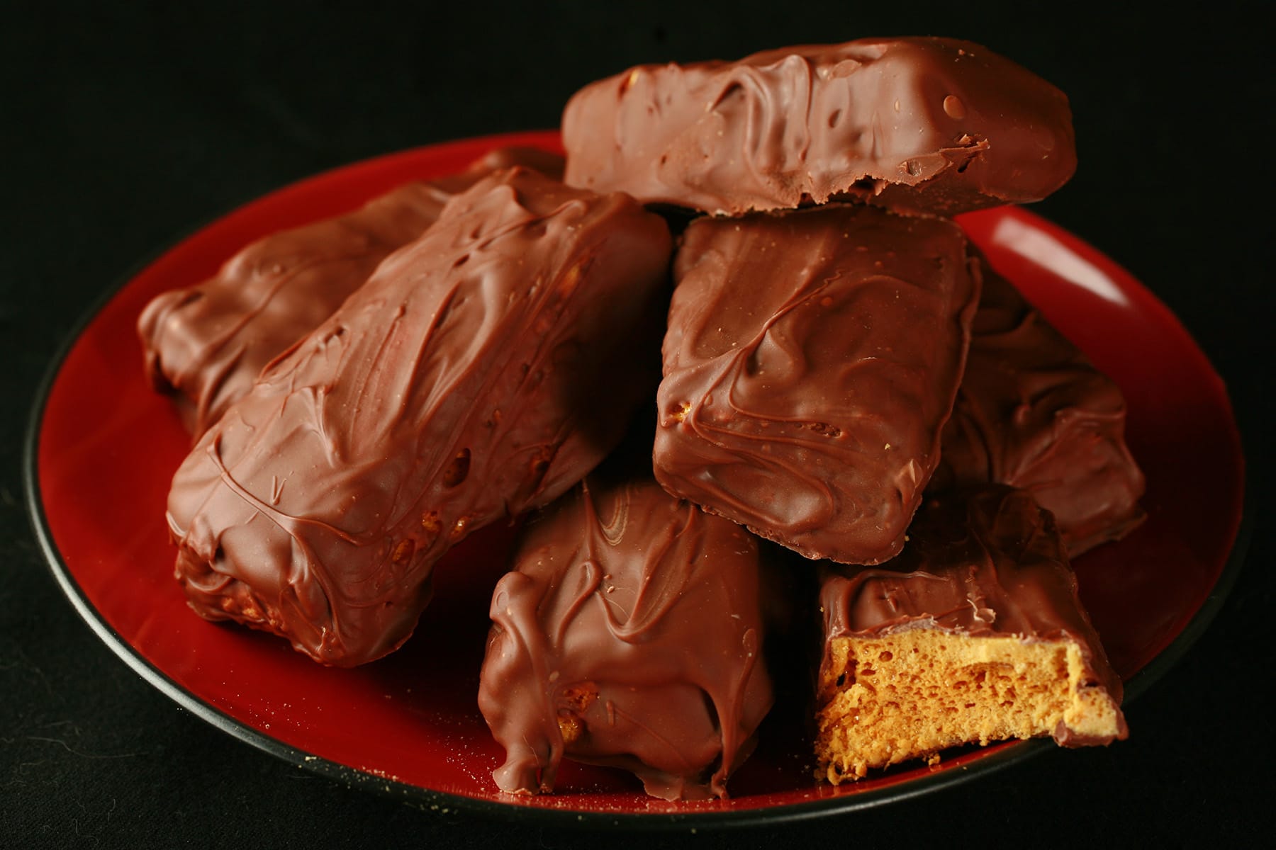 A small red plate is piled high with homemade crunchie bars. One is broken in half to reveal the honeycomb toffee inside.