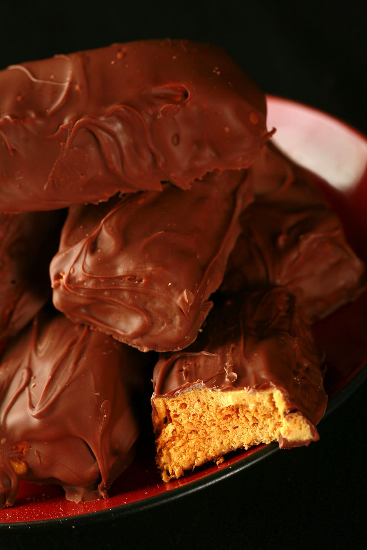 A small red plate is piled high with homemade crunchie bars. One is broken in half to reveal the sponge toffee inside.