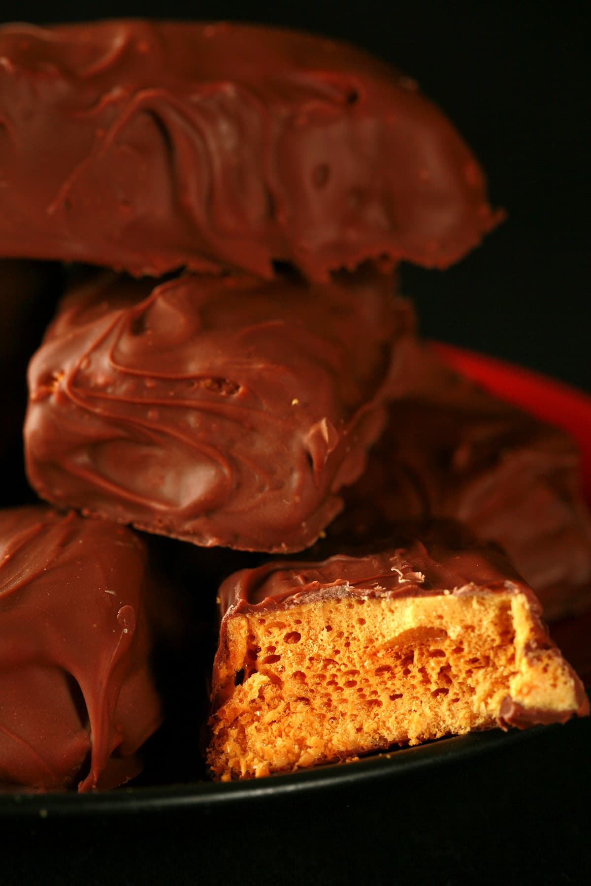 A small red plate is piled high with homemade crunchie bars. One is broken in half to reveal the sponge toffee inside.