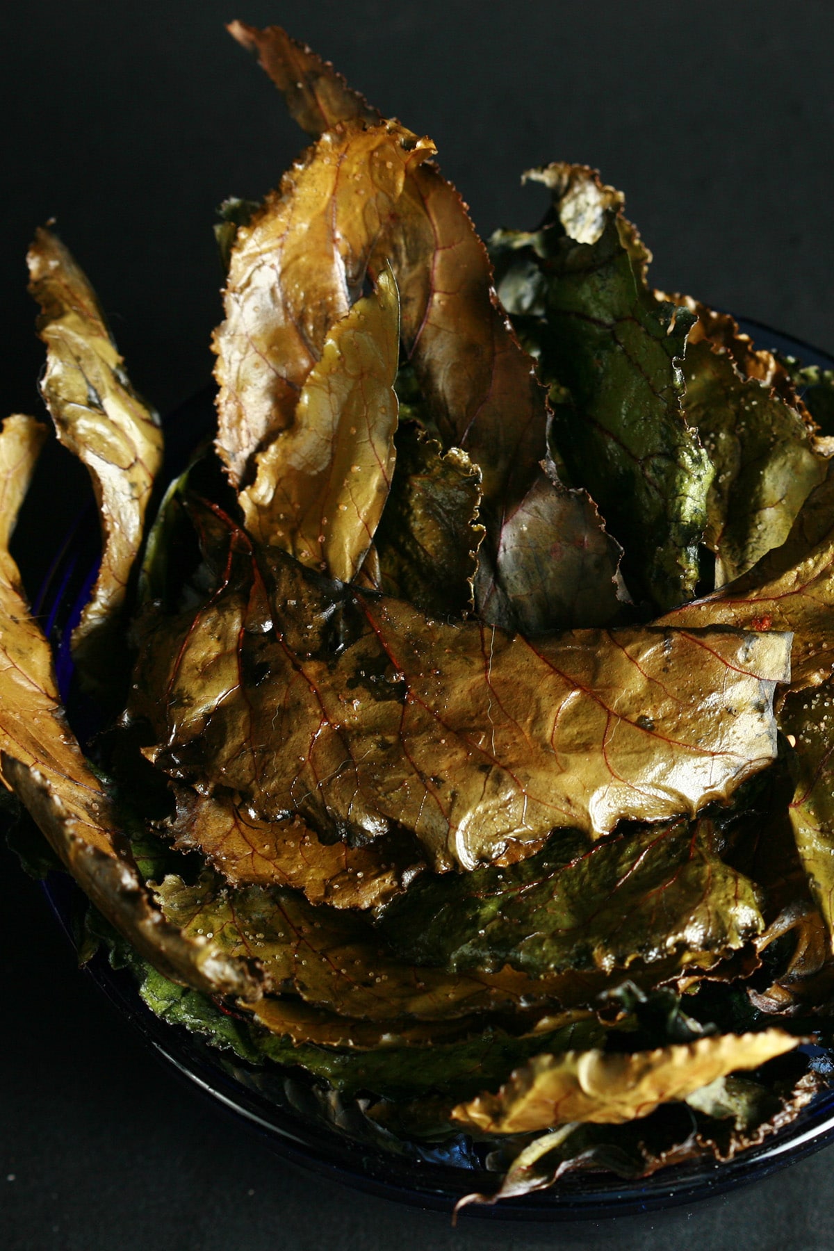 A bowl of roasted beet green chips - deep shades of greens and browns, with beautiful red veining.