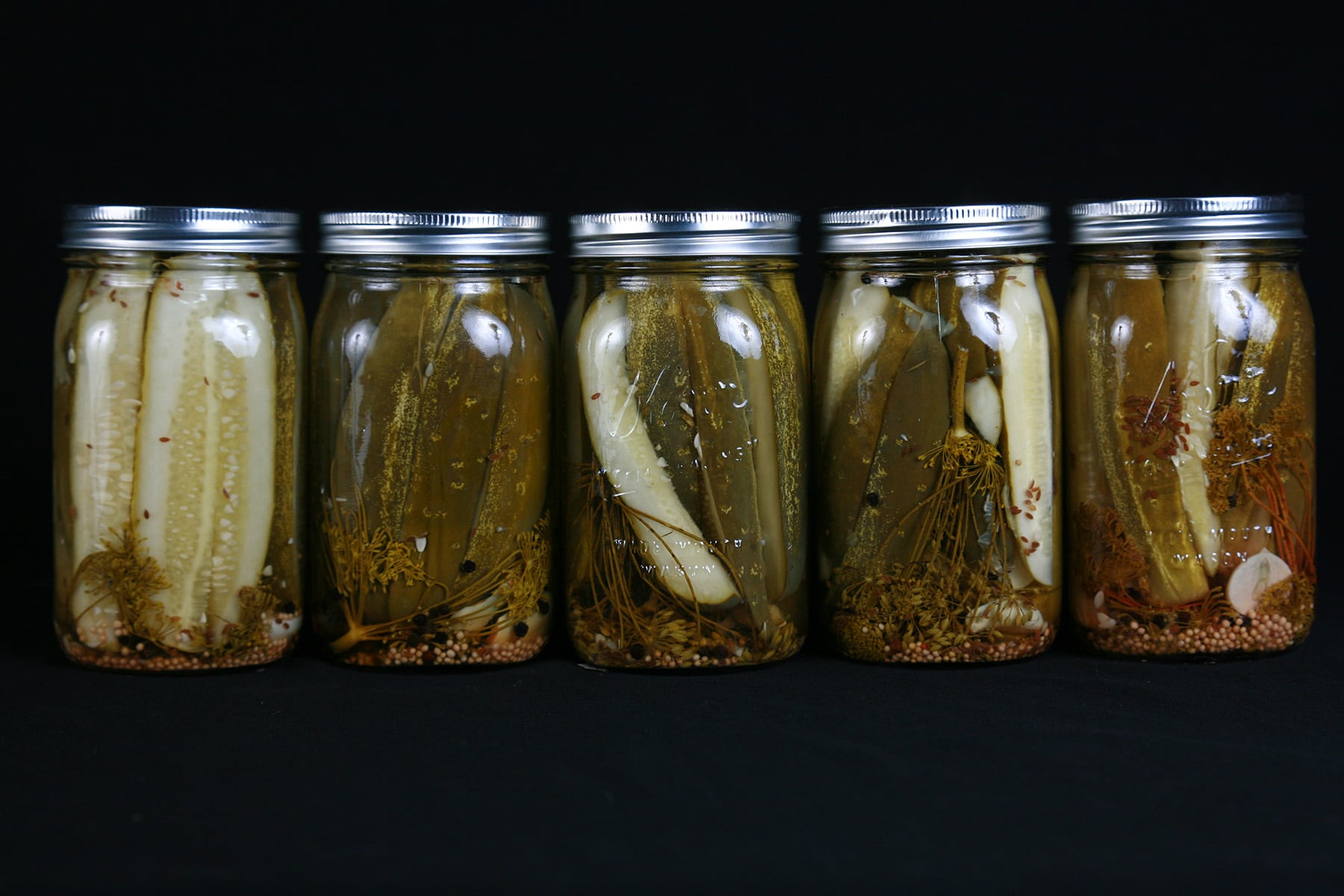 A line of 5 large jars of homemade dill pickles.