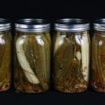 A line of 4 large jars of homemade dill pickles.