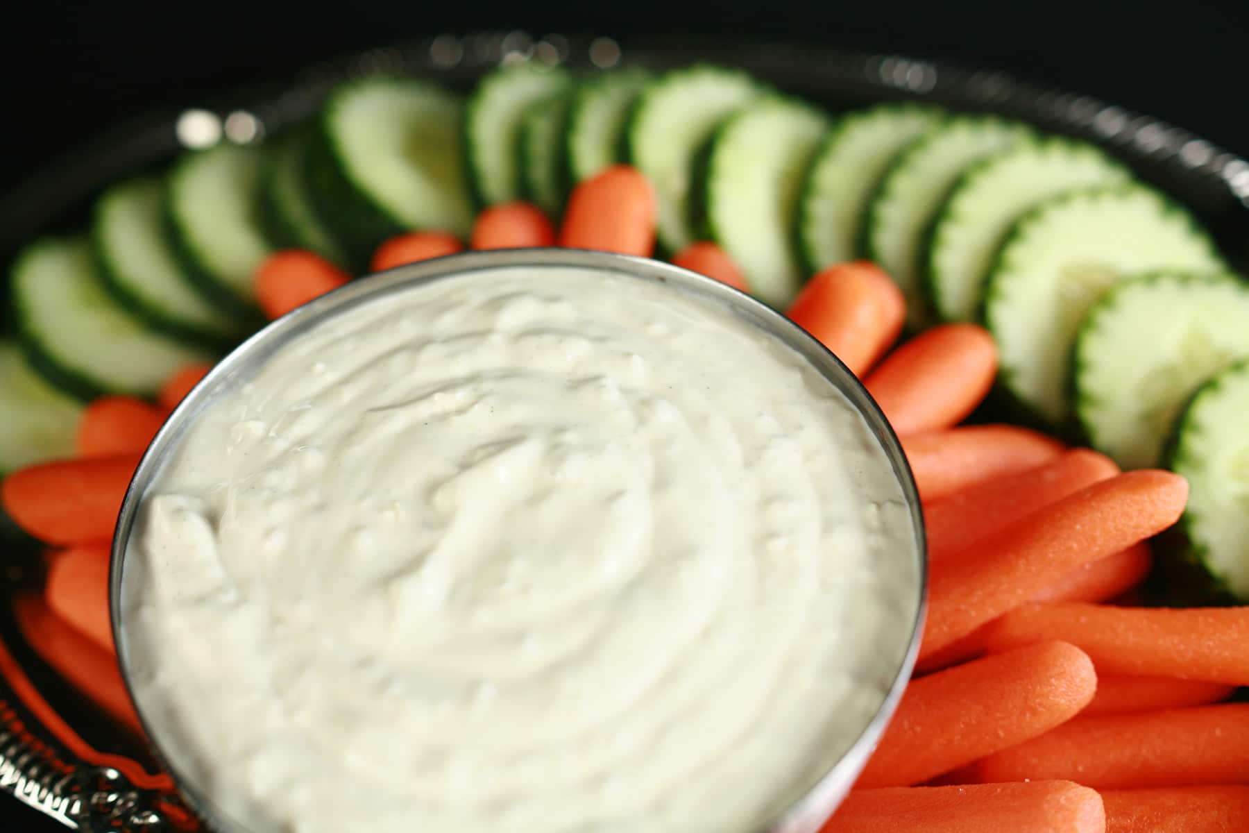 A bowl of ginger wasabi dip, surrounded by cucumber slices and baby carrots.