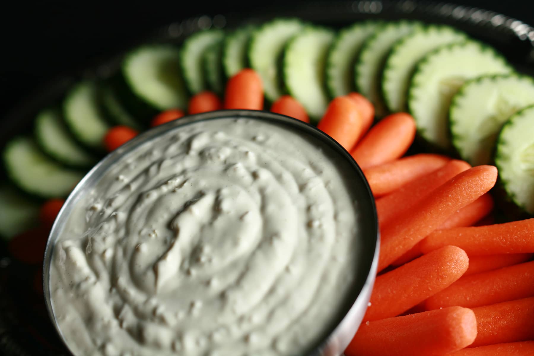 A bowl of wasabi ginger dip, surrounded by cucumber slices and baby carrots.