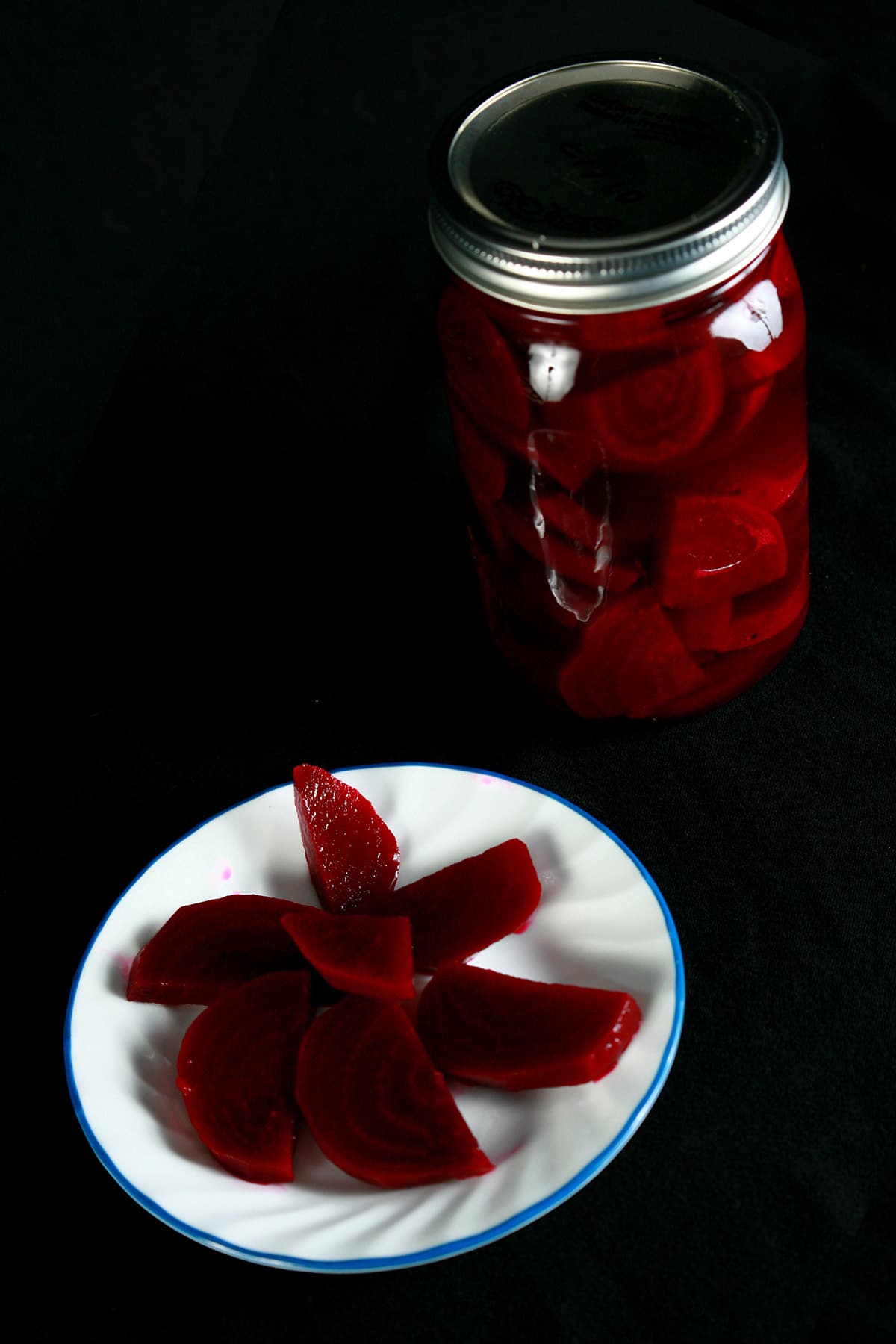 A jar of pickled beets, behind a plate with beet pickles on it.
