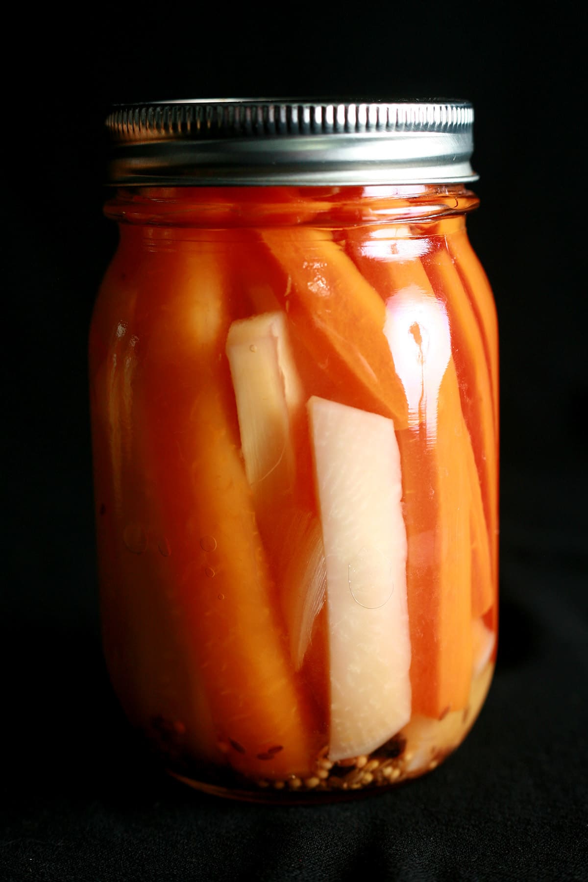 A jar of mixed root vegetable pickles. Spears of carrot, parsnip, and turnip are visible.