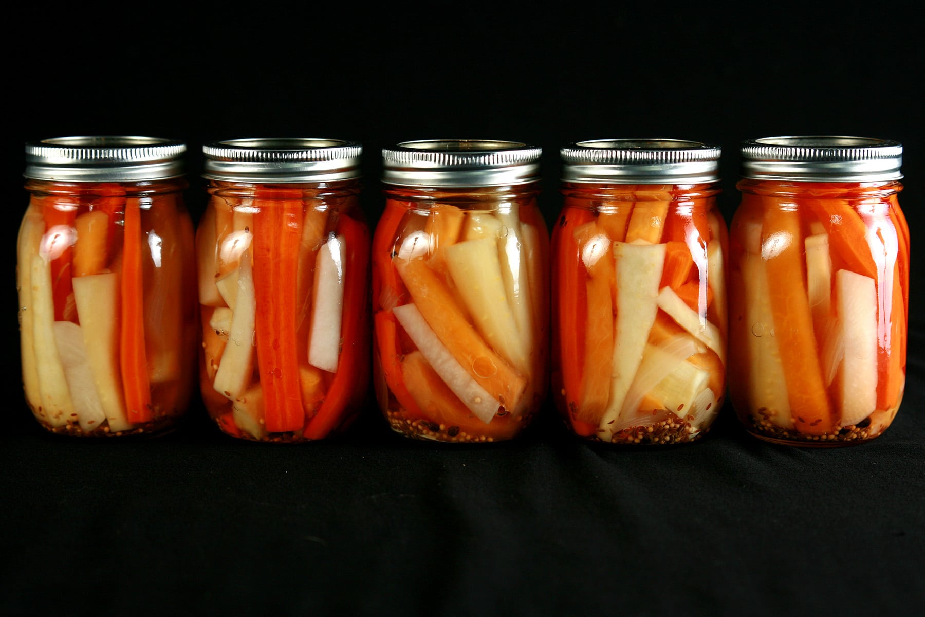 5 jars of mixed root vegetable pickles. Spears of carrot, parsnip, and turnip are visible.