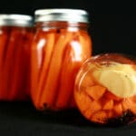 3 jars of homemade pickled carrots. One is on its side, slices of fresh ginger are visible on the bottom.