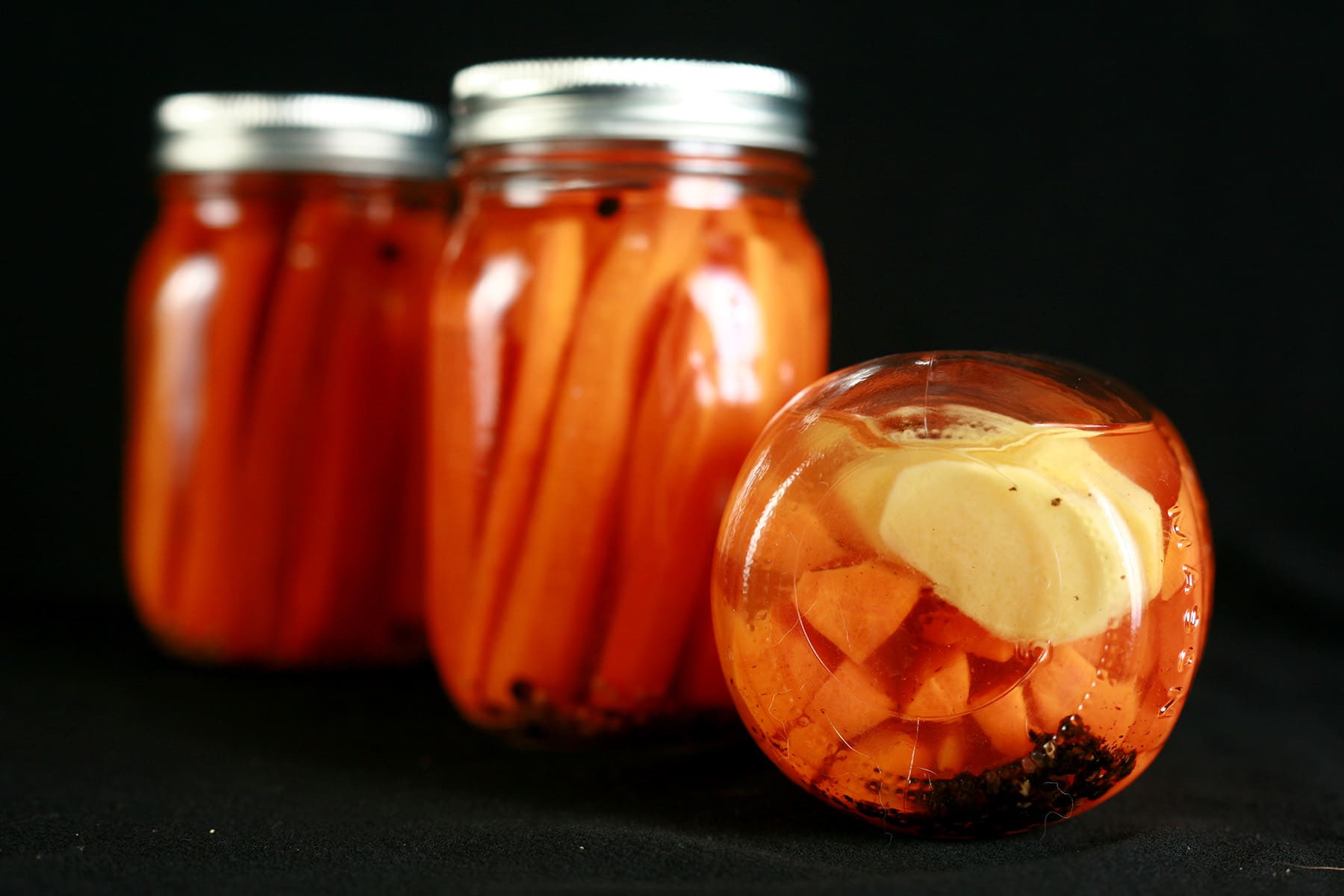 3 jars of homemade pickled carrots. One is on its side, slices of fresh ginger are visible on the bottom.