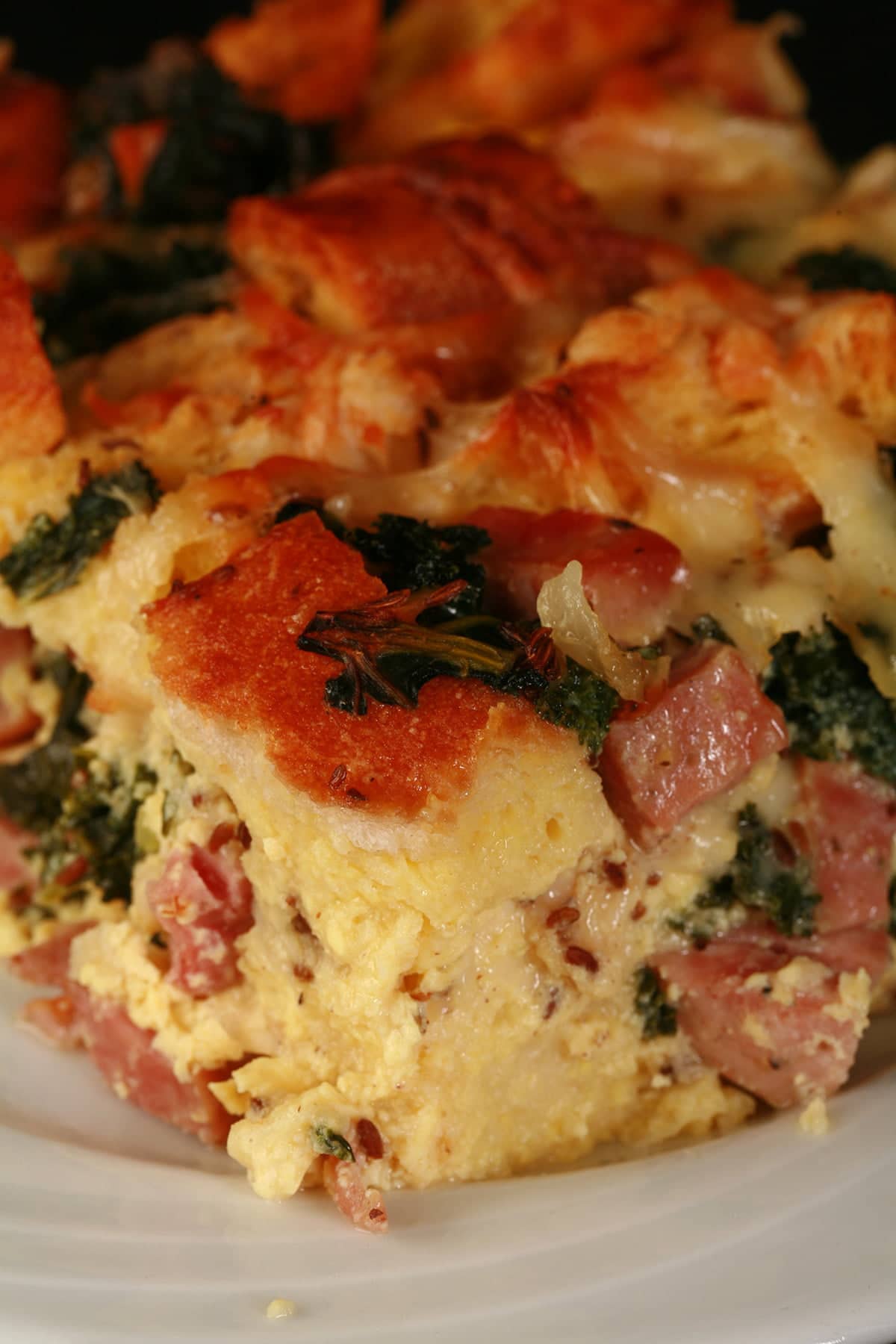 A large square serving of ham, kale, and swiss strata on a white plate.