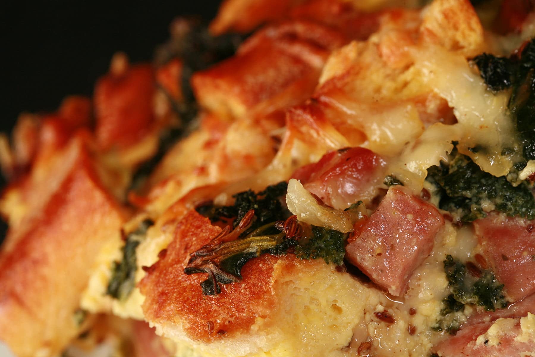A large square serving of ham, kale, and swiss strata on a white plate.