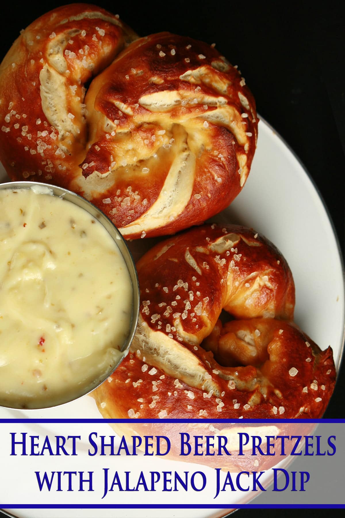 Close up photo of 2 heart shaped pretzels and a small bowl of cheese dip. It is labeled with "Heart Shaped Beer Pretzels with Jalapeno Jack Dip" in blue writing.