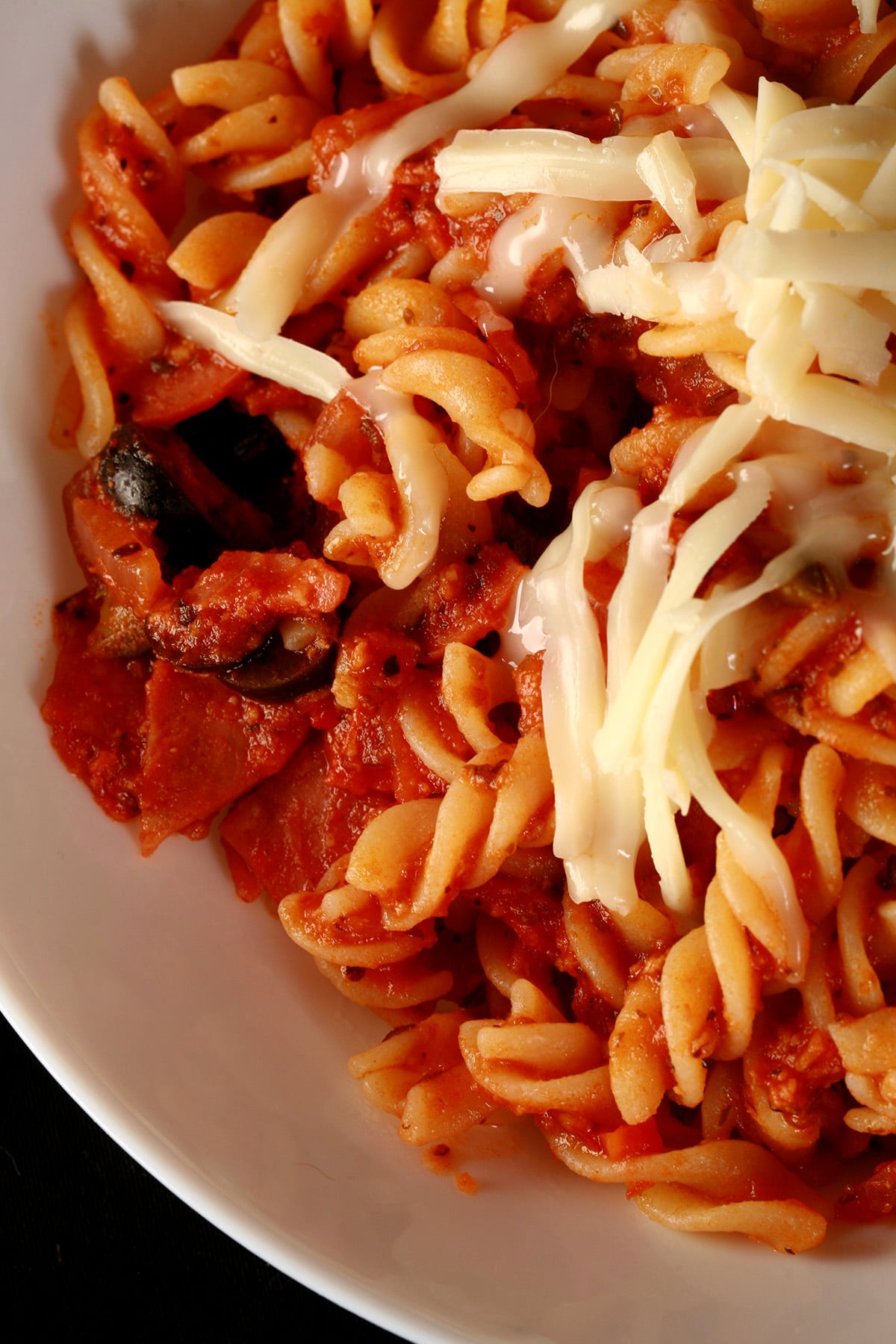 A bowl of pasta in red sauce, with bits of pepperoni and sliced black olives visible. There is shredded mozzarella on top - Pasta Alla Porters.