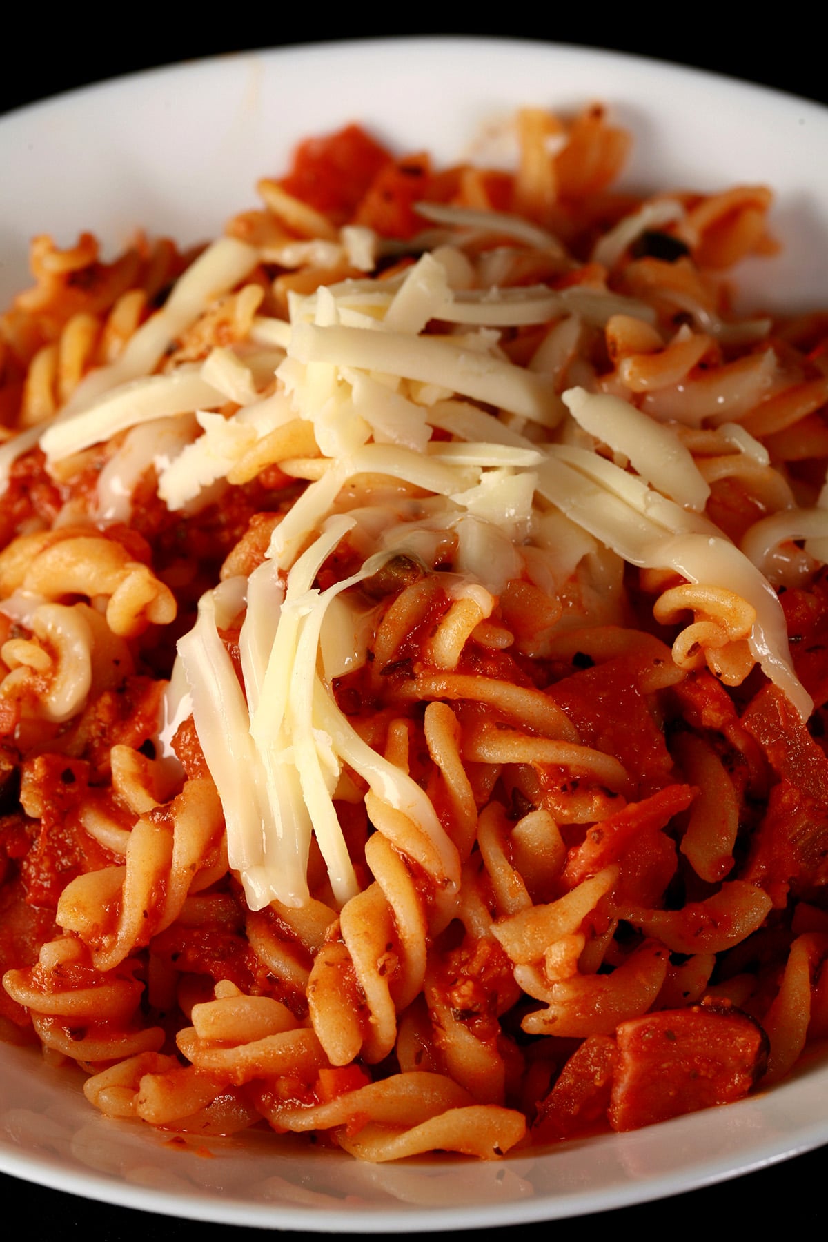 A bowl of pasta in red sauce, with bits of pepperoni and sliced black olives visible.