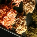 A parchment lined baking sheet with mounds of red, white, and green coloured fresh linguini on it.