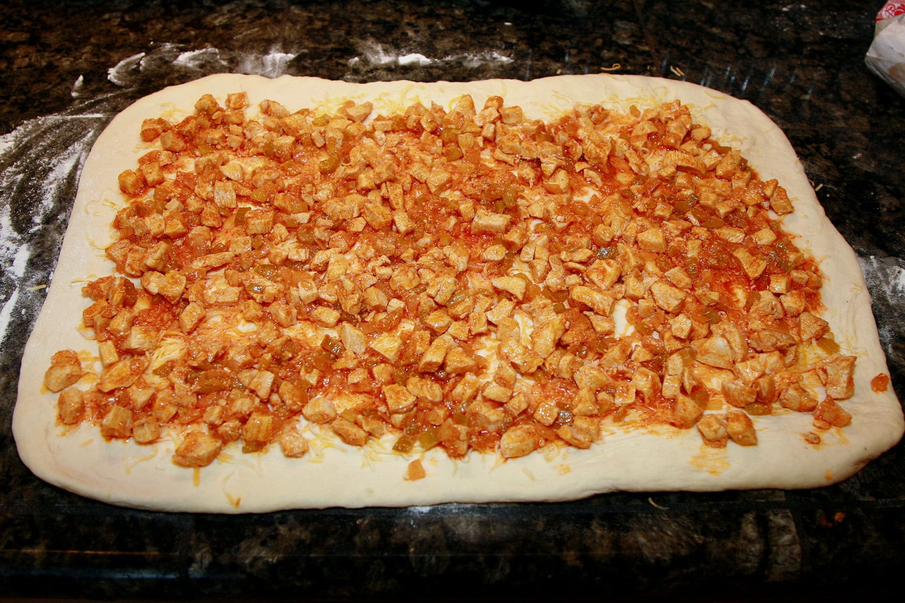 A rectangle of dough is spead with finely chopped chicken in buffalo sauce.