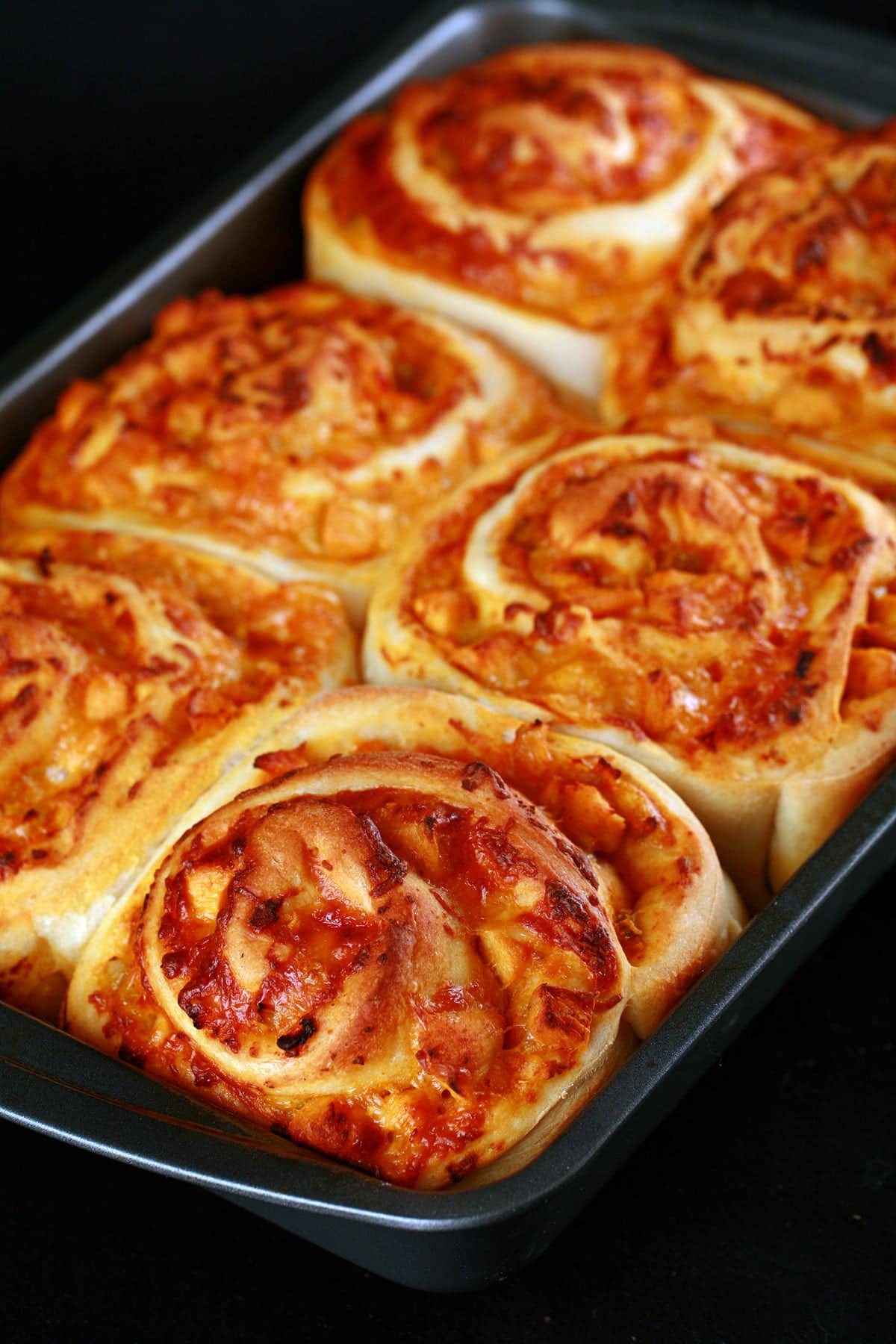 A pan of 6 baked buffalo chicken buns. They resemble cinnamon buns, but with a buffalo chicken and cheese filling.