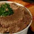 A pot of cretons - a French Canadian pork pate - in a small white ramekin, next to slices of toast.